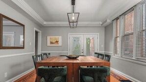 A dining room with a wooden table, green upholstered chairs, a hanging light fixture, and a framed picture on the wall. - The Reserve ~ 5BR Fun! Hot Tub, Fire Pit, Deck, Walkable To Bardstown Rd (Louisville)