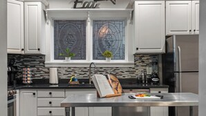 A modern kitchen with white cabinets, a stainless steel refrigerator, and a large window with stained glass. - The Reserve ~ 5BR Fun! Hot Tub, Fire Pit, Deck, Walkable To Bardstown Rd (Louisville)