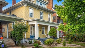 A two-story yellow house with a porch, brick chimneys, and a well-maintained garden. - The Reserve ~ 5BR Fun! Hot Tub, Fire Pit, Deck, Walkable To Bardstown Rd (Louisville)
