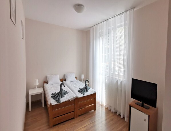 A bedroom with two wooden beds, a white nightstand, a TV on a stand, and sheer curtains.