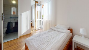 Une chambre à coucher avec un lit, une table de chevet et une salle de bain visible à travers une porte ouverte.