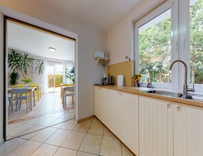 Een keuken met een raam, een spoelbak en een eethoek met stoelen en een tafel.