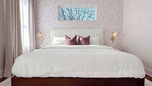 Quarto com cama grande, papel de parede estampado, janela com vista para uma árvore e duas luminárias de parede.