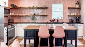Uma cozinha moderna com azulejos rosa, bancadas de madeira e dois banquetes rosa.