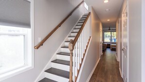 A staircase with wooden handrails and dark steps, leading to a room with a bench and a radiator. - Lakeside Bliss- Close to Highmark Stadium, home of the Bills! (Angola)