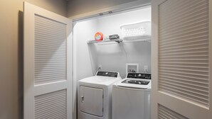A compact laundry room with two white front-loading washers and dryers, a shelf with laundry detergent, and a power outlet. - Lakeside Bliss- Close to Highmark Stadium, home of the Bills! (Angola)