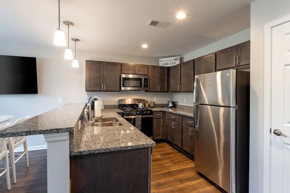 A modern kitchen with granite countertops, stainless steel appliances, and dark wooden cabinets. - Lakeside Bliss- Close to Highmark Stadium, home of the Bills! (Angola)