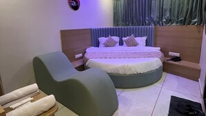 Une chambre à coucher moderne avec un lit aux lignes courbes, un fauteuil vert et une petite table d’appoint en bois.