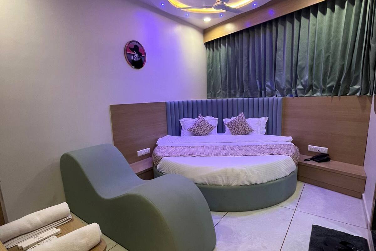 Ein modernes Schlafzimmer mit einem gewölbten Bett, einem grünen Sessel und einem kleinen Holfnachtkästchen.
