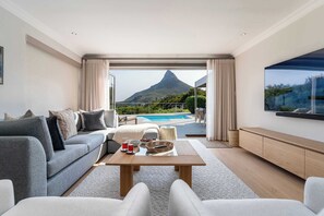 A modern living room with a sofa, coffee table, and a view of a mountain and pool. - 180 Views, Pool, Modern, Camps Bay - Nura Townhouse (Cape Town)