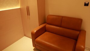 Una habitación moderna con un sofá de cuero marrón, un armario blanco y una lámpara fijada a la pared.