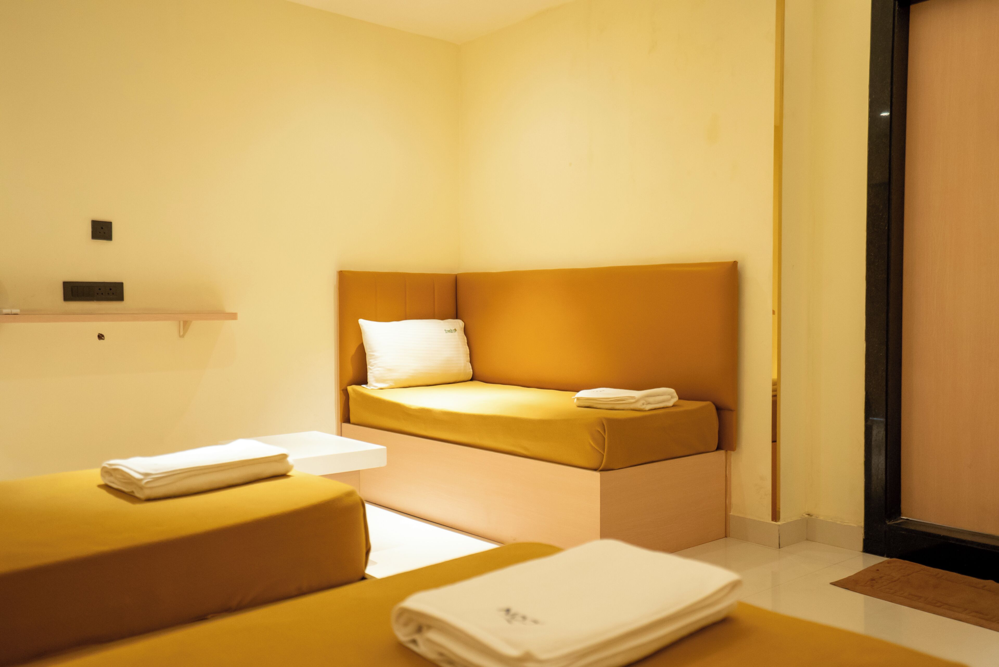 A compact hotel room with a single bed, a small bedside table, and a bench.