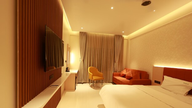 Una habitación de hotel moderna con una cama grande, un televisor de pantalla plana montado en la pared, un escritorio con una silla y un sofá.