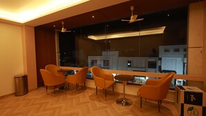 Una habitación moderna con un ventanal grande, suelo de madera y sillas anaranjadas alrededor de una mesita.