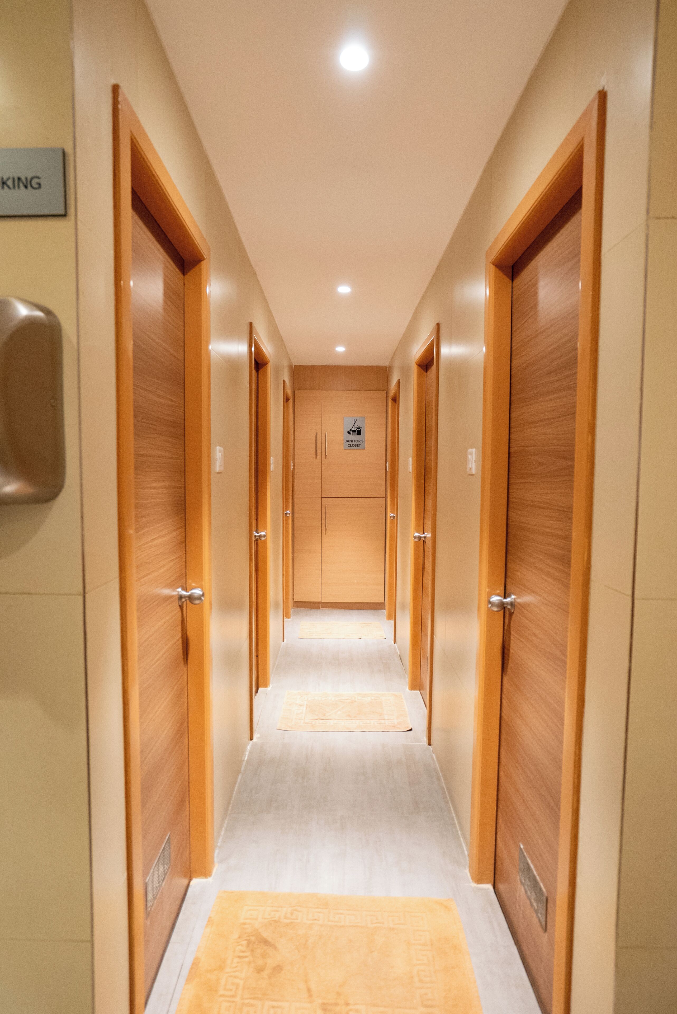 A hotel corridor with wooden doors, a sign indicating a janitor's closet, and a light fixture on the ceiling.
