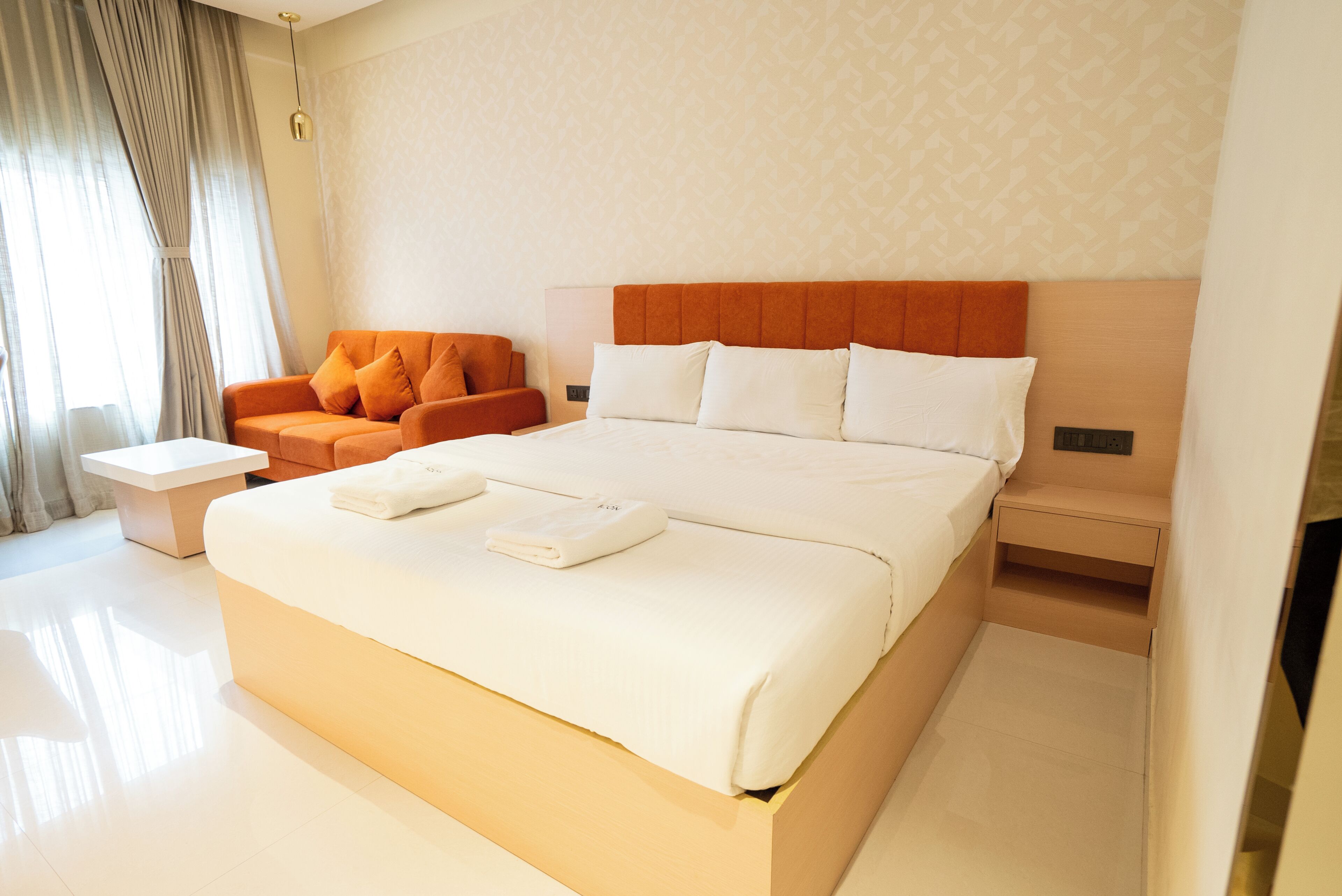 Quarto de hotel com cama grande, sofá, mesa de cabeceira e luminária na parede.