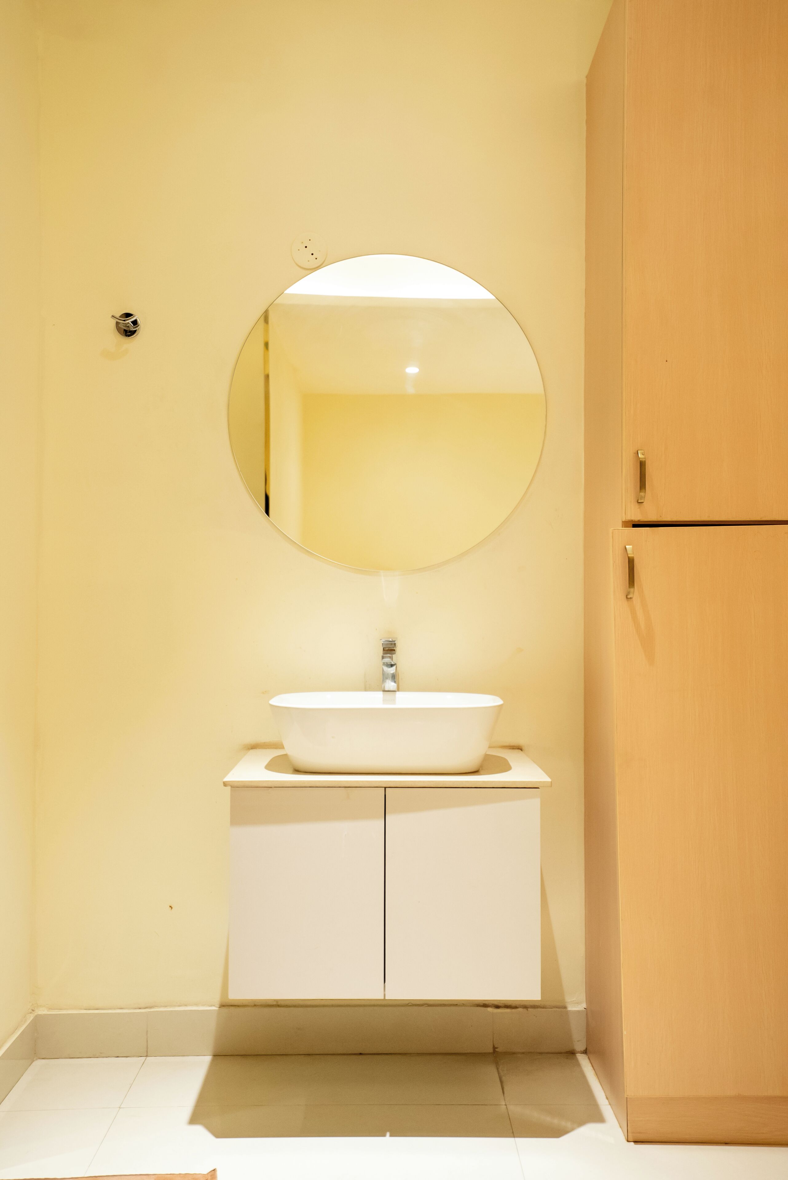 A bathroom with a white sink, a round mirror, and a wooden cabinet.