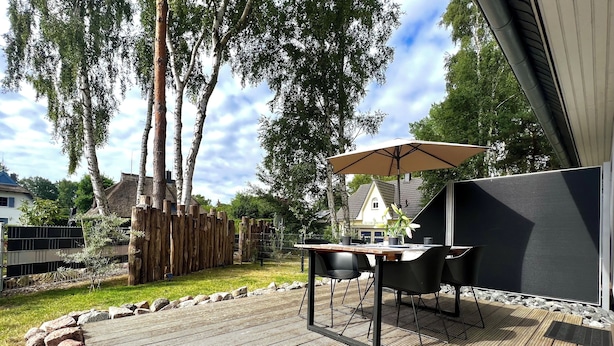 A wooden deck with a table and chairs, a large umbrella, and a TV screen.