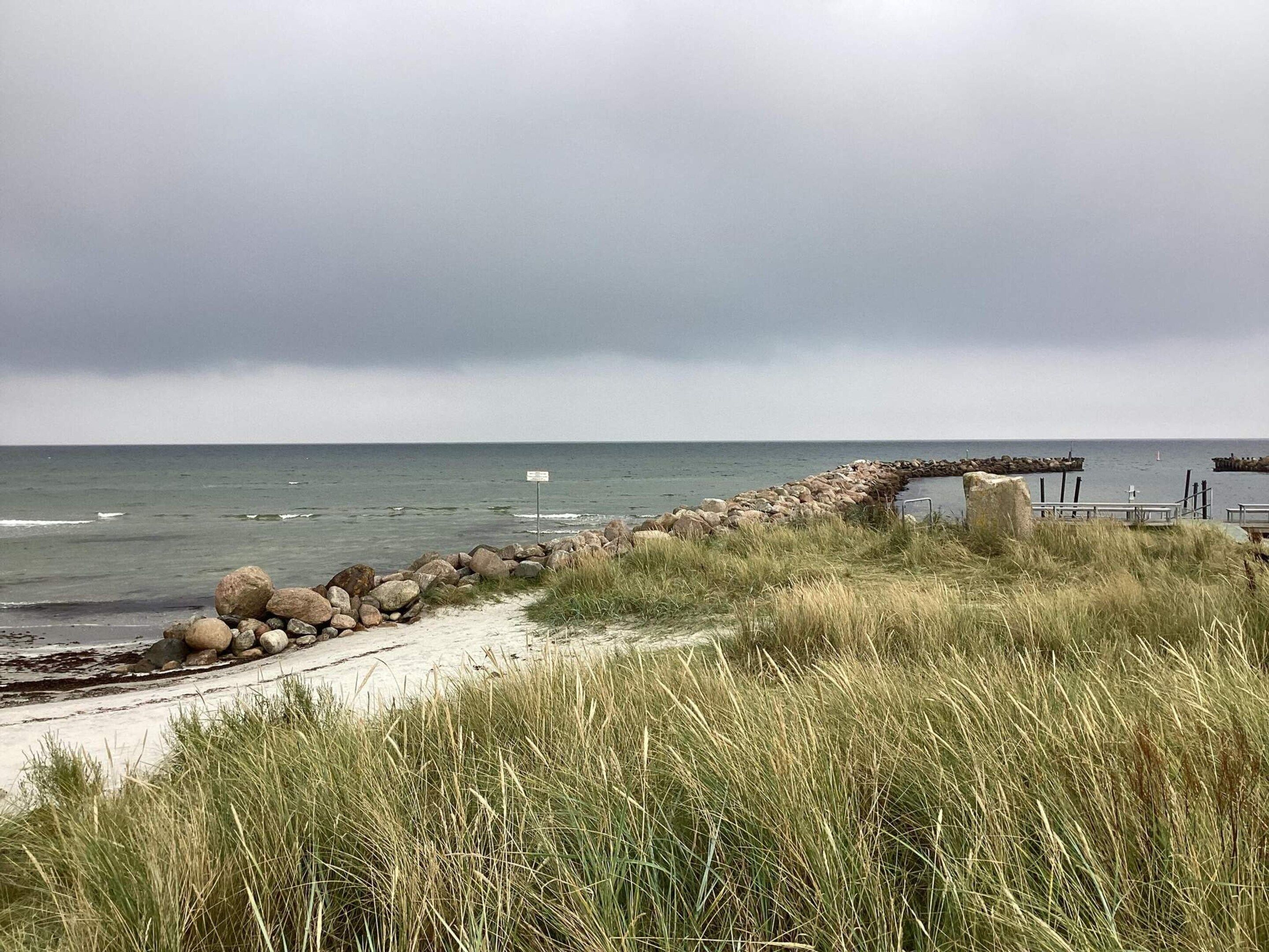 A coastal path with a stone wall, grassy dunes, and a view of the sea.