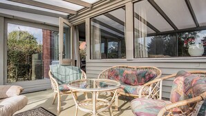 Une terrasse ensoleillée, meublée de meubles en osier, avec une table en verre et un tapis à motifs.