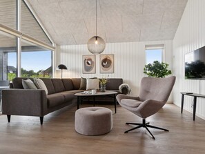 A modern living room with a sectional sofa, a round ottoman, a single chair, a coffee table, and a pendant light.