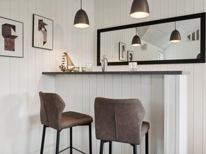 A bar area with two stools, a mirror above the counter, and framed artwork on the wall.