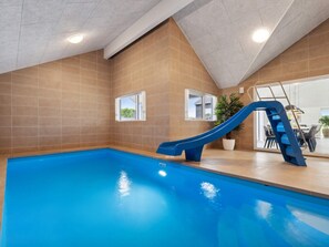 An indoor swimming pool with a blue slide, tiled walls, and a window.