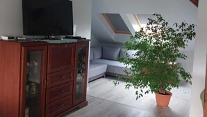A modern living room with a flat-screen TV, wooden cabinet, grey sofa, and a potted plant. - Apartment in Sopot Near Monte Cassino Street (Sopot)