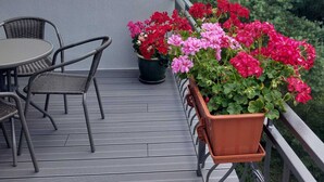 A balcony with a table and chairs, surrounded by potted plants with red and pink flowers. - Apartment in Sopot Near Monte Cassino Street (Sopot)