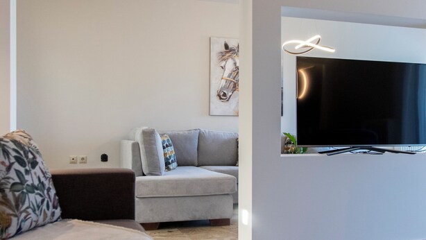 A modern living room with a large flat-screen TV mounted on the wall, a sofa, and a coffee table.