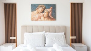 A neatly made bed with white linens and two pillows, a painting of a couple above it, and wooden paneling on the walls.