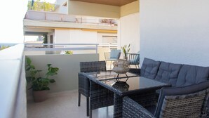 A balcony with wicker furniture, a glass table, and a potted plant.