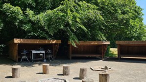 A rustic outdoor area with wooden structures, a barbecue setup, and fire pits. - 2 Person Holiday Park Home in Lemvig (Lemvig)