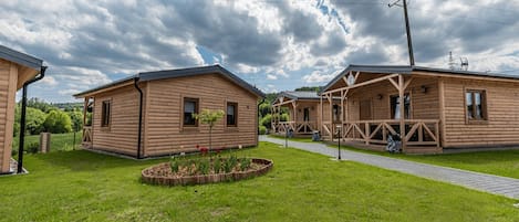 A row of wooden cabins with a paved walkway between them, surrounded by a grassy area.