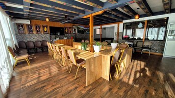 Un'ampia sala da pranzo con un lungo tavolo in legno e sedie, un angolo cottura con una griglia, e un muro in pietra ornato da quadri.