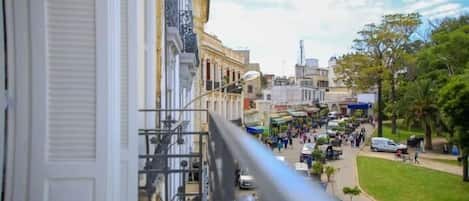 A street view from a balcony with buildings, a pedestrian area, and parked cars.
