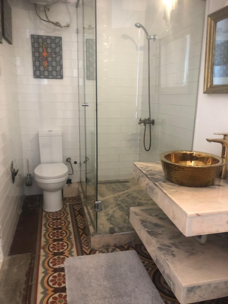 A bathroom with a toilet, a shower, a marble sink, and a decorative bowl.