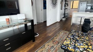 A modern living room with a flat-screen TV, a black entertainment unit, a patterned rug, and a dining area with a glass table. - Lalla radia (Tangier)