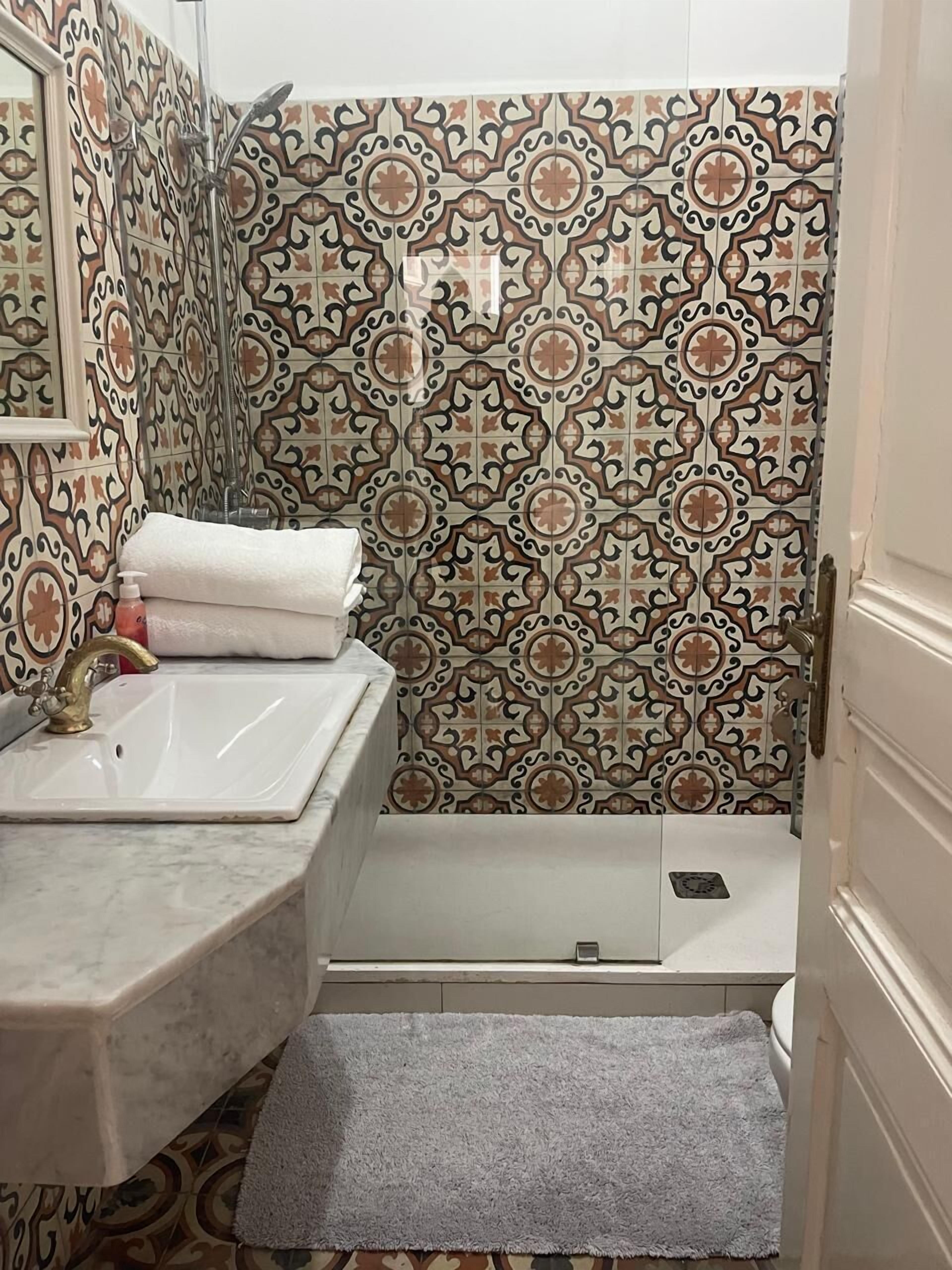 Een badkamer met een wastafel, spiegel, douche en betegelde vloer.