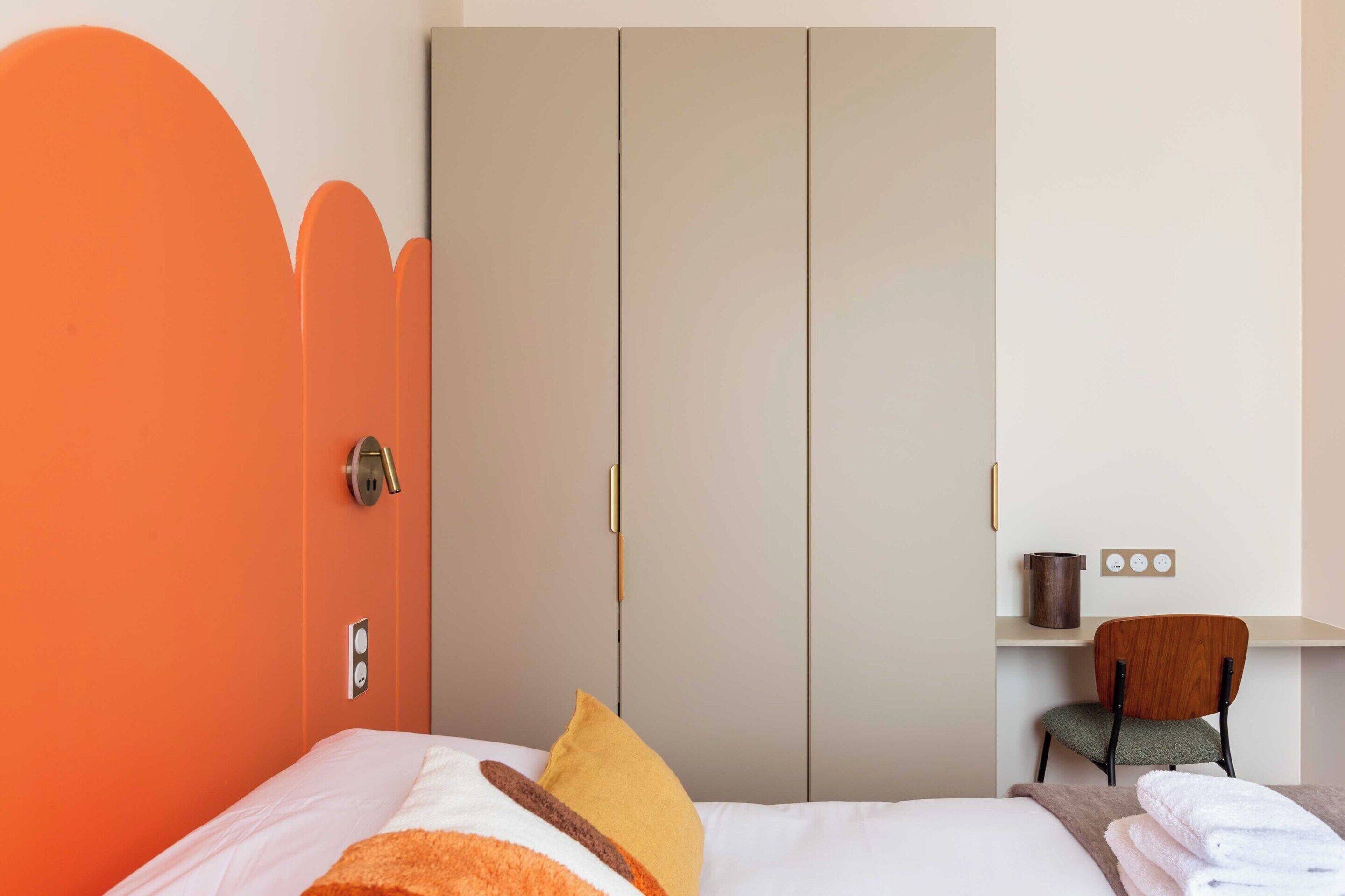 A hotel room with a bed, a chair, a wardrobe, and a small table with a kettle.