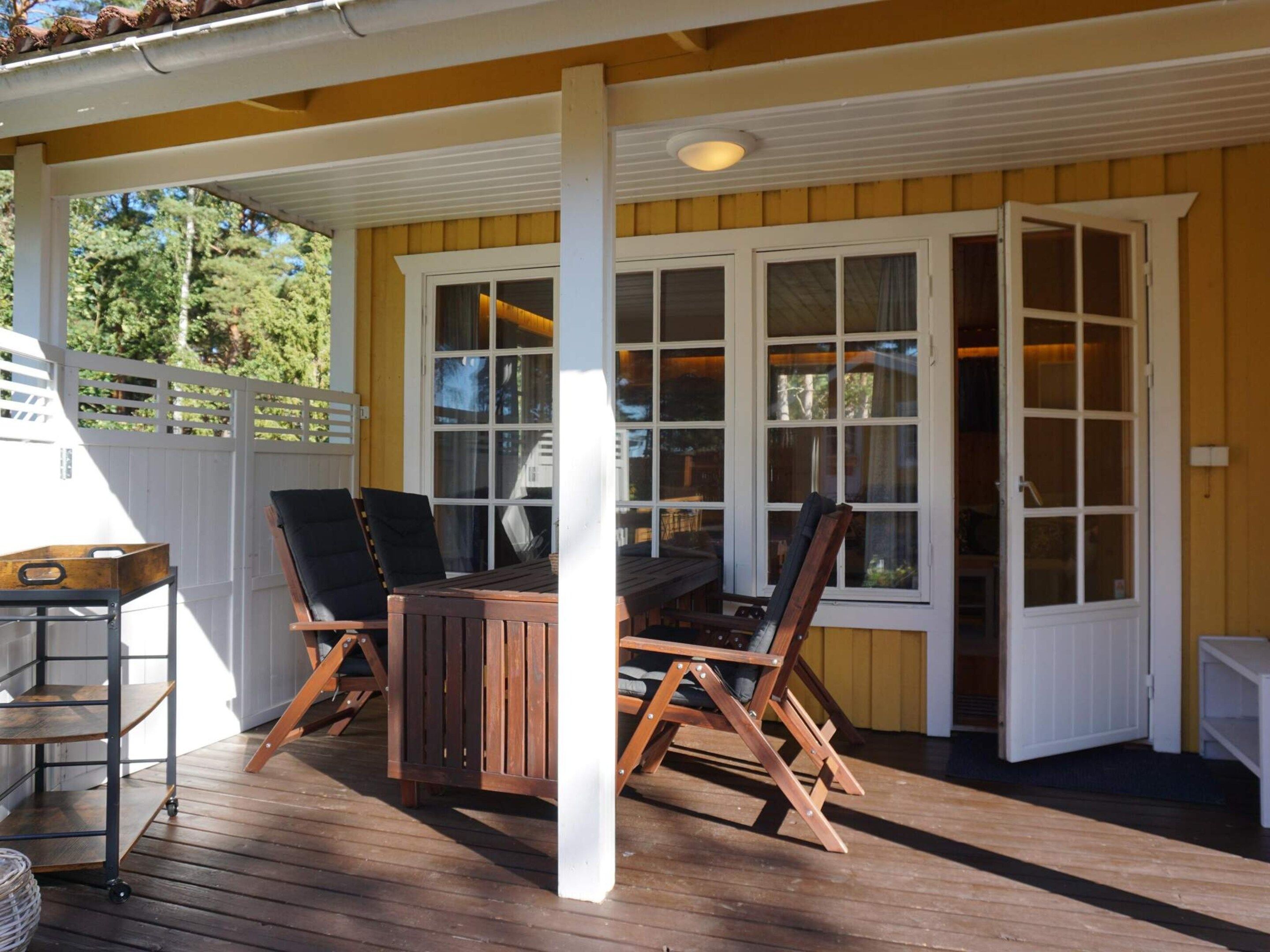 A covered outdoor area with a wooden deck, a table with chairs, and a white-framed window.