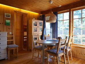 A wooden interior with a dining table, chairs, a cabinet, and a window with a view.