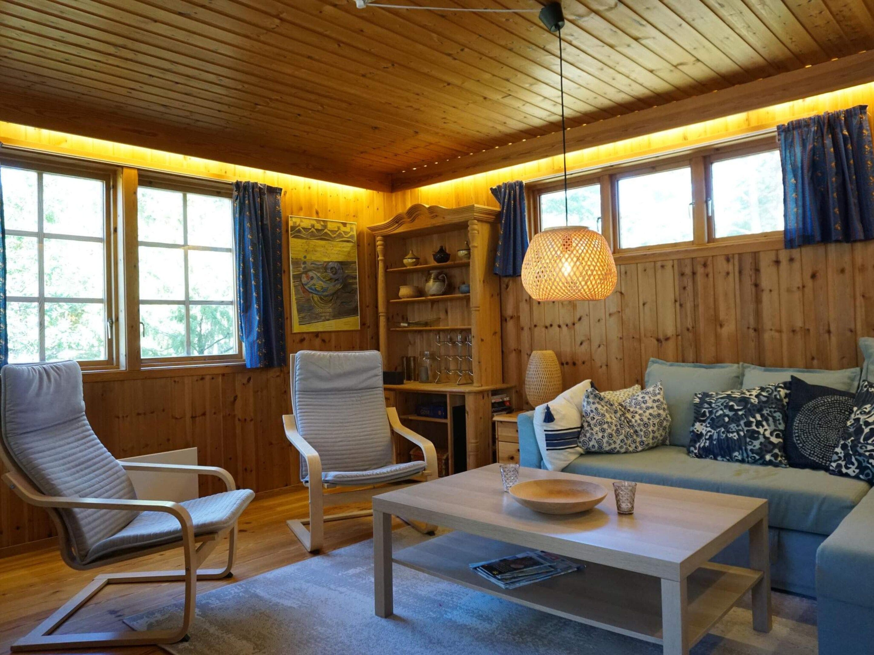 Et hyggeligt rum med trævægge, en sofa, to stole, et bord og en hængende lampe.