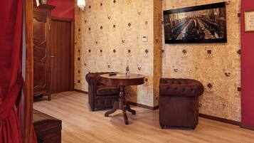 Um quarto com uma mesa redonda de madeira, duas poltronas de couro marrom, um armário de madeira e papel de parede estampado.