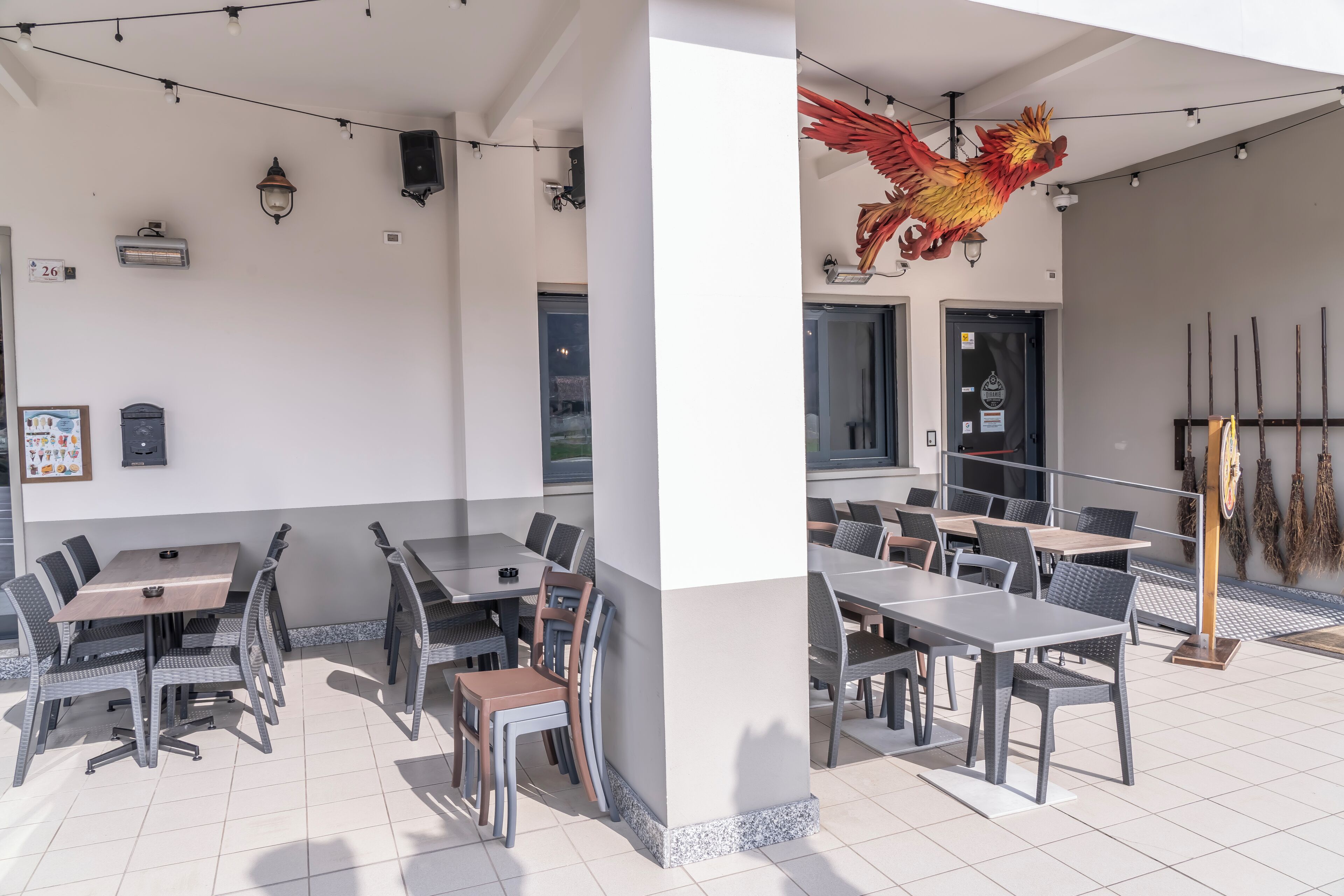 An outdoor dining area with tables and chairs, a decorative rooster, and a wall-mounted speaker.