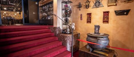 A staircase with red carpet leading to a room with a large, ornate stove and shelves with various items.