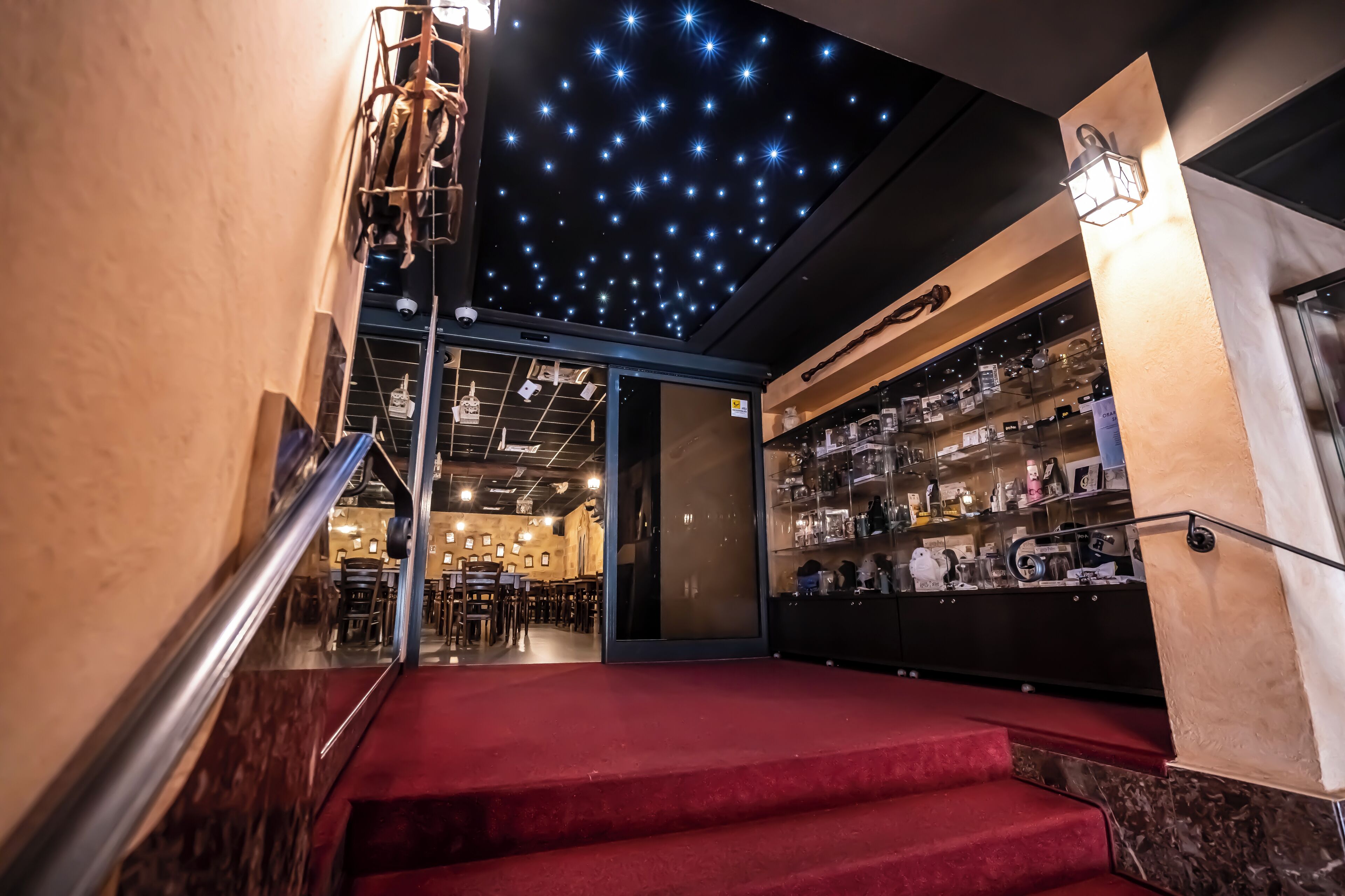 Un escalier recouvert d’une moquette rouge mène à un espace bar où l’on trouve des étagères remplies de bouteilles et un plafond constellé d’étoiles.