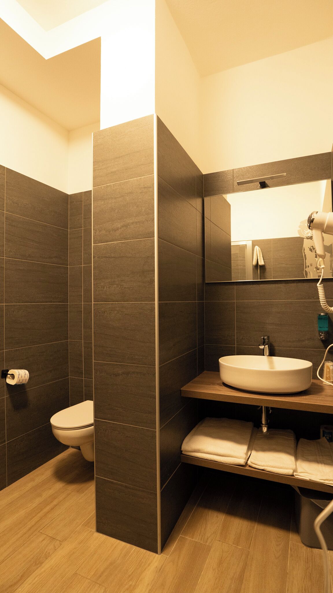 Un baño moderno con azulejos oscuros, un inodoro, un lavabo y un perchero para toallas.