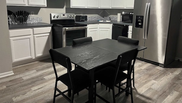 Una cocina moderna con armarios blancos, electrodomésticos de acero inoxidable y una mesa de comedor con sillas.