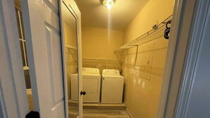Un cuarto de lavandería con dos lavadoras, un tendedero y un cubo de basura.